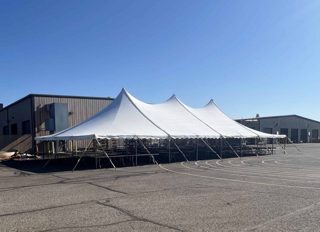 A large white event tent is set up on concrete with a clear blue sky overhead.