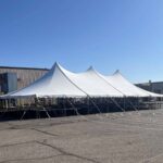 A large white event tent is set up on concrete with a clear blue sky overhead.