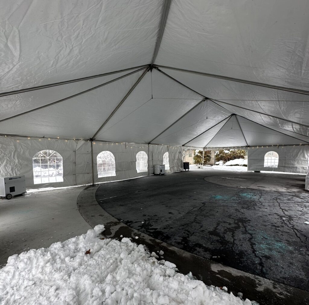 A large white tent interior on a snowy day with windows and string lights. Snow piles outside create a cozy contrast to the spacious setup.