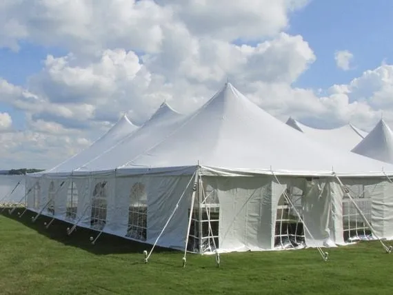 A large white event tent with pointed peaks stands on green grass under a blue sky with fluffy clouds.