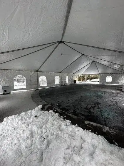 A large white tent interior on a snowy day with windows and string lights. Snow piles outside create a cozy contrast to the spacious setup.